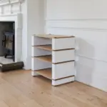 Blok Stax 2G White fireplace Stax 2G Base carrying three shelves in natural ash and satin white beside a fireplace